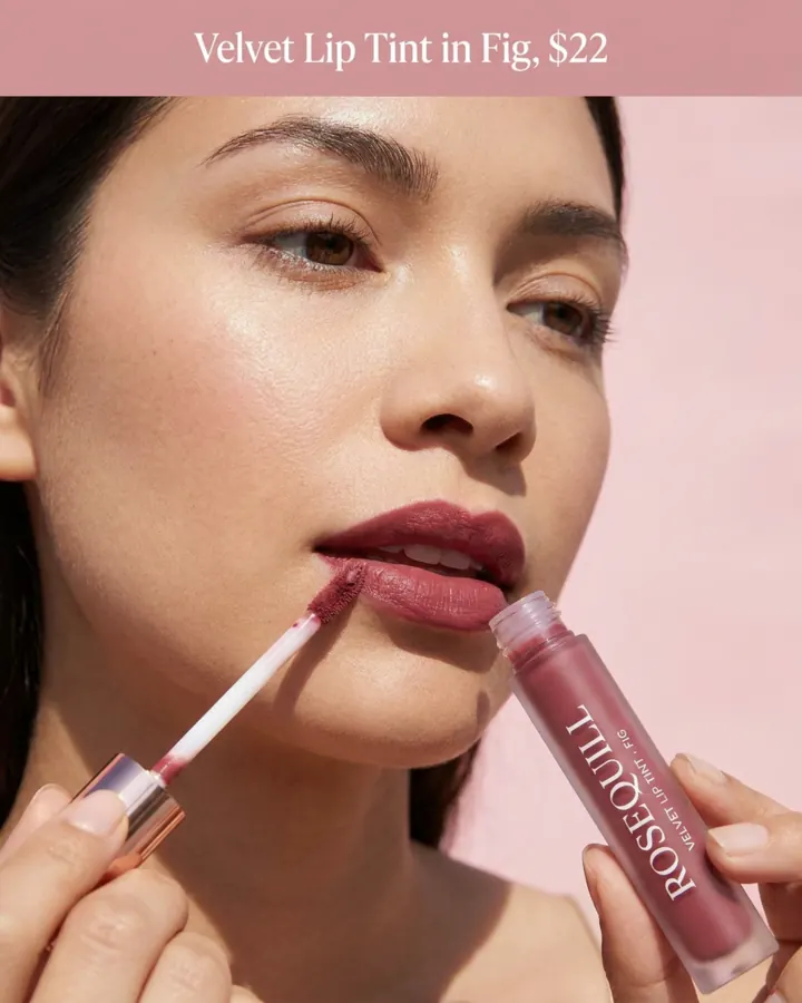 AI output for the fifth prompt: a close-up of a woman applying berry lip colour with a doe-foot wand while holding the Rosequill tube upside down in her other hand, under a band reading Velvet Lip Tint in Fig, $22.